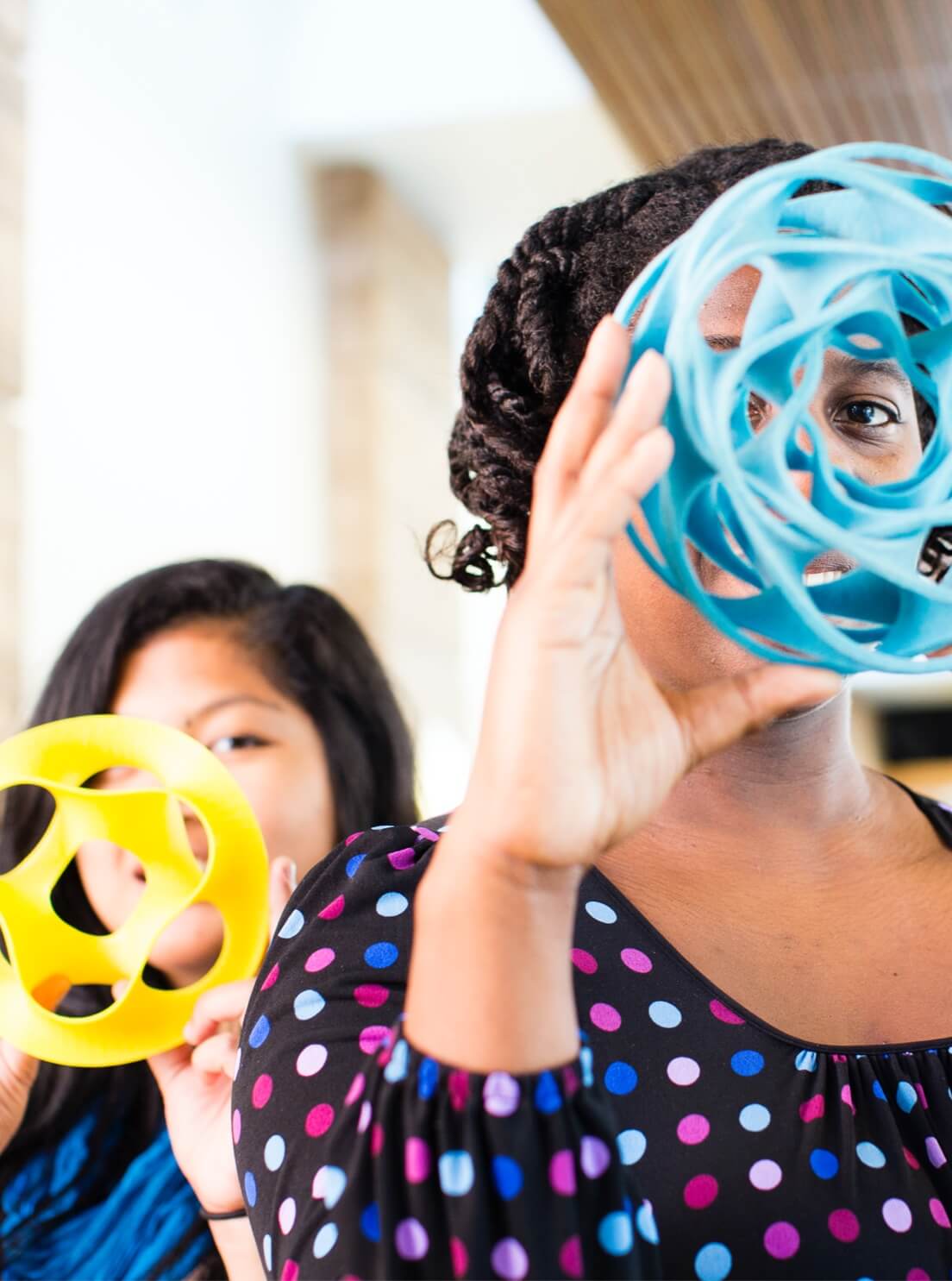 2 women holding colorful geometric sculptures