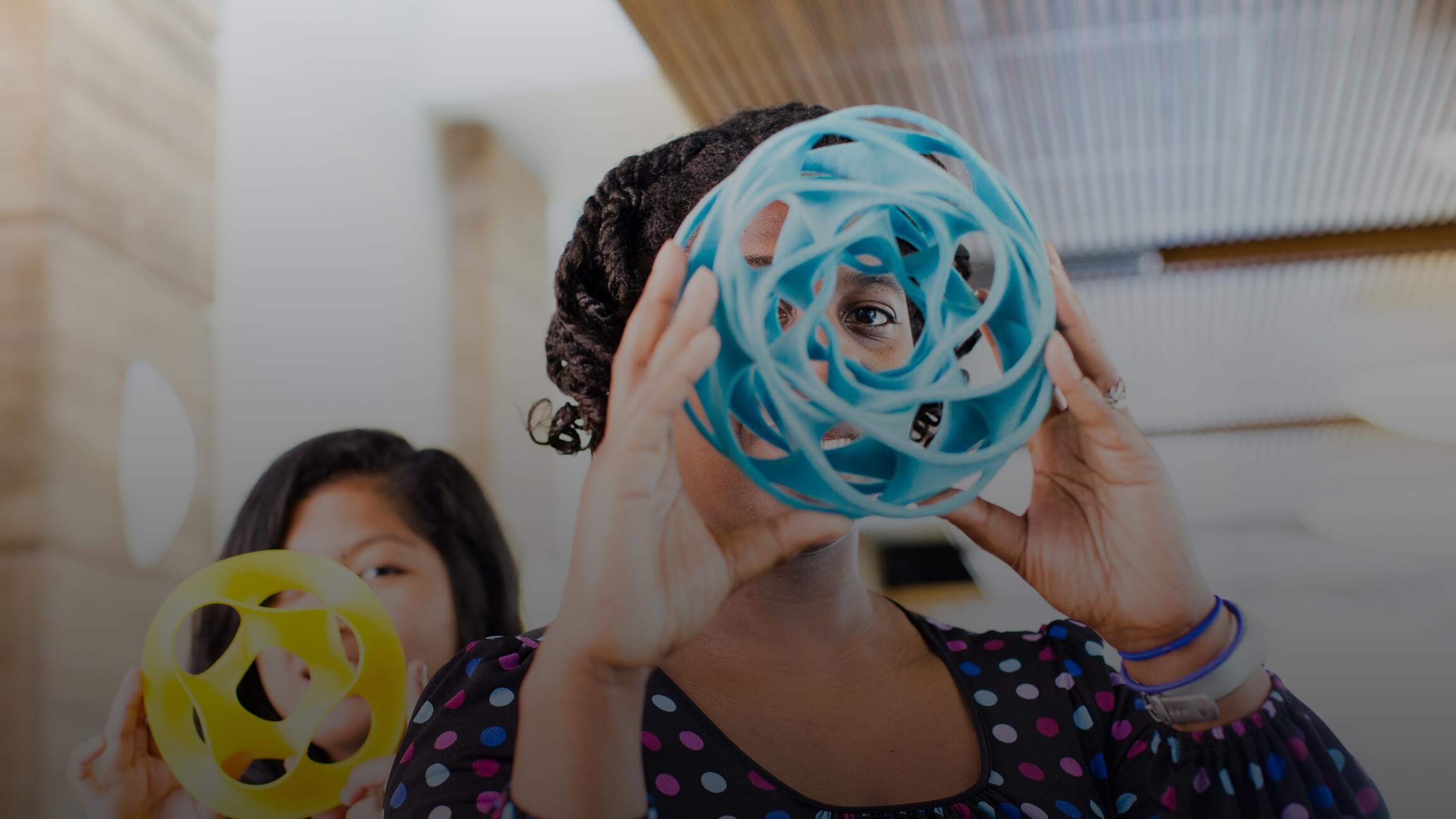 2 women holding colorful geometric sculptures